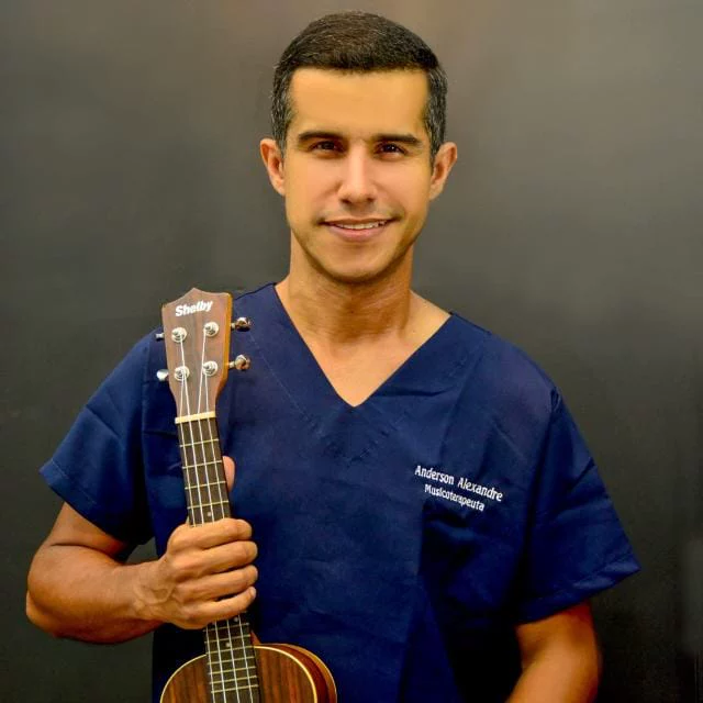 Anderson Alexandre, musicoterapeuta, de uniforme azul, segurando um ukulele